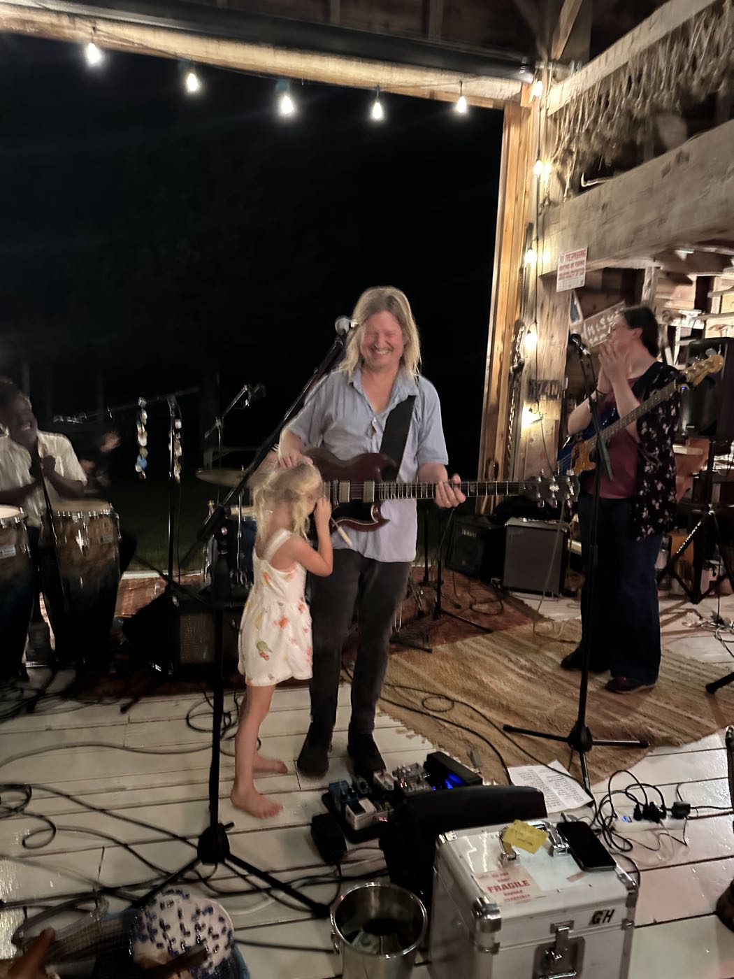 Greg Humphreys on stage at night under string lights with a small child beside him